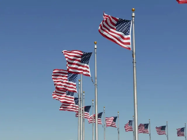 Row of American flags flying on flagpoles against a blue sky