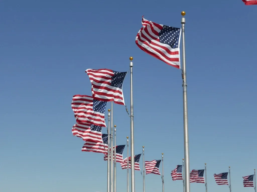 Row of American flags flying on flagpoles against a blue sky