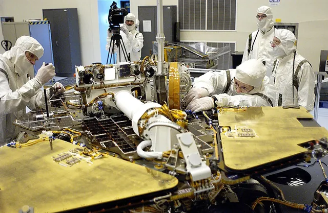 Technicians in clean-room suits working on circuit boards inside a Mars rover