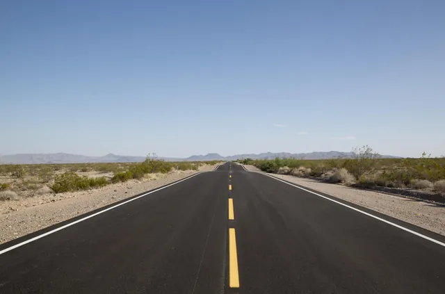 Empty two-lane highway running straight into the Mojave Desert