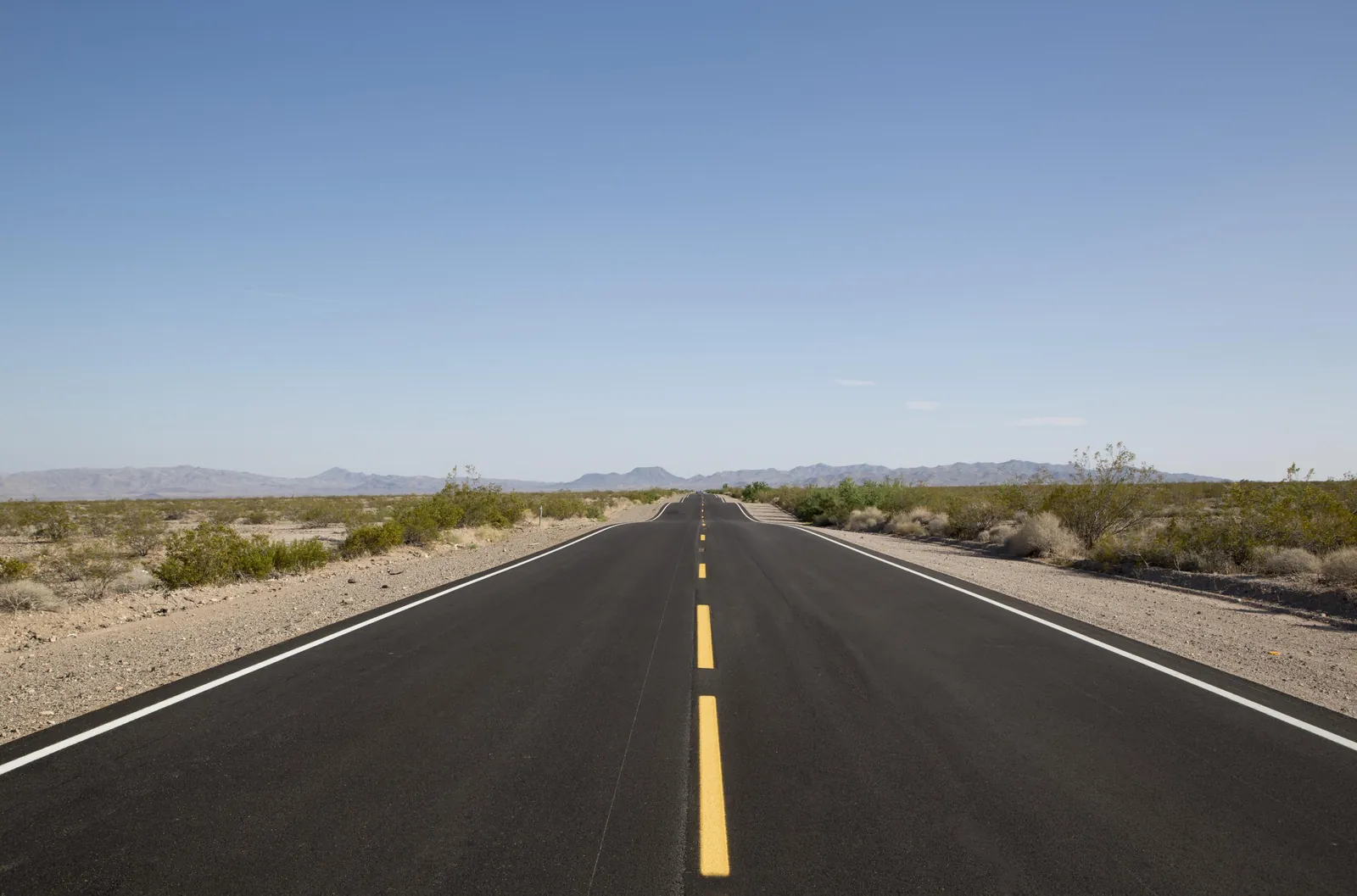 Empty two-lane highway running straight into the Mojave Desert