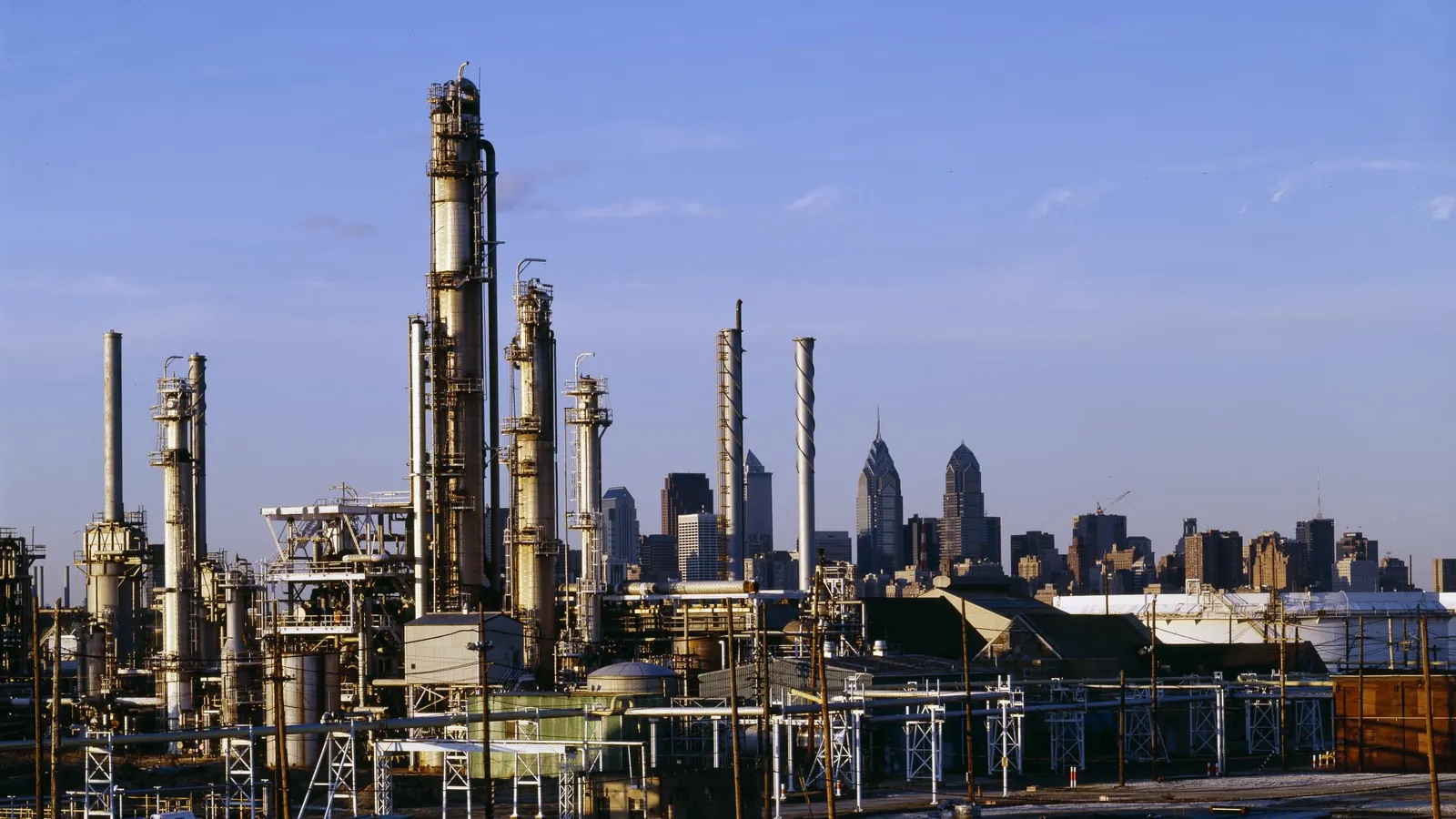 Oil refinery towers and pipes with a city skyline in the distance