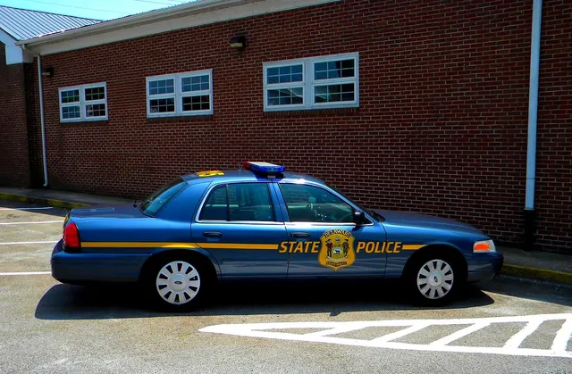 A blue state police patrol car parked beside a brick building